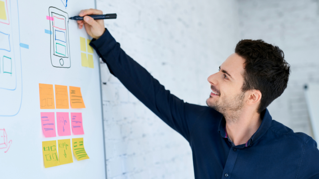Designer sketching mobile app wireframes and sticky notes on a whiteboard
