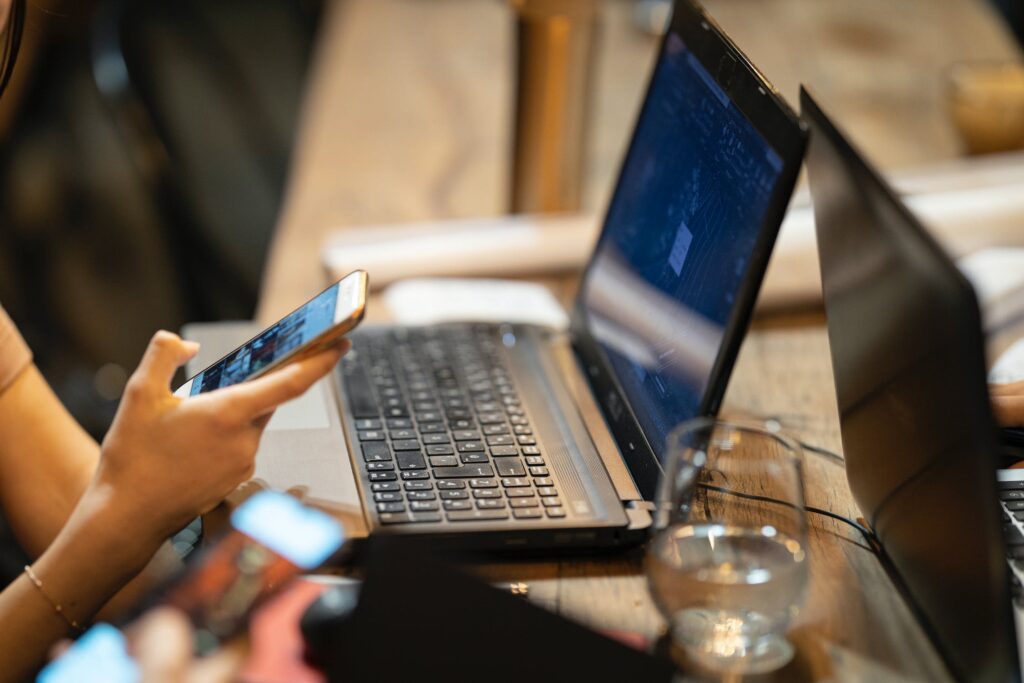 Two people working at a table with two laptops open, one showing a dark code editor, while one person checks a phone