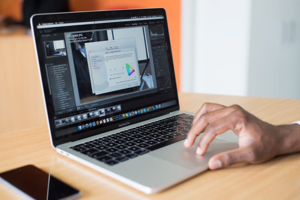 A laptop screen showing photo-editing software open in a colour-correction dialog, with a phone resting on the desk beside it